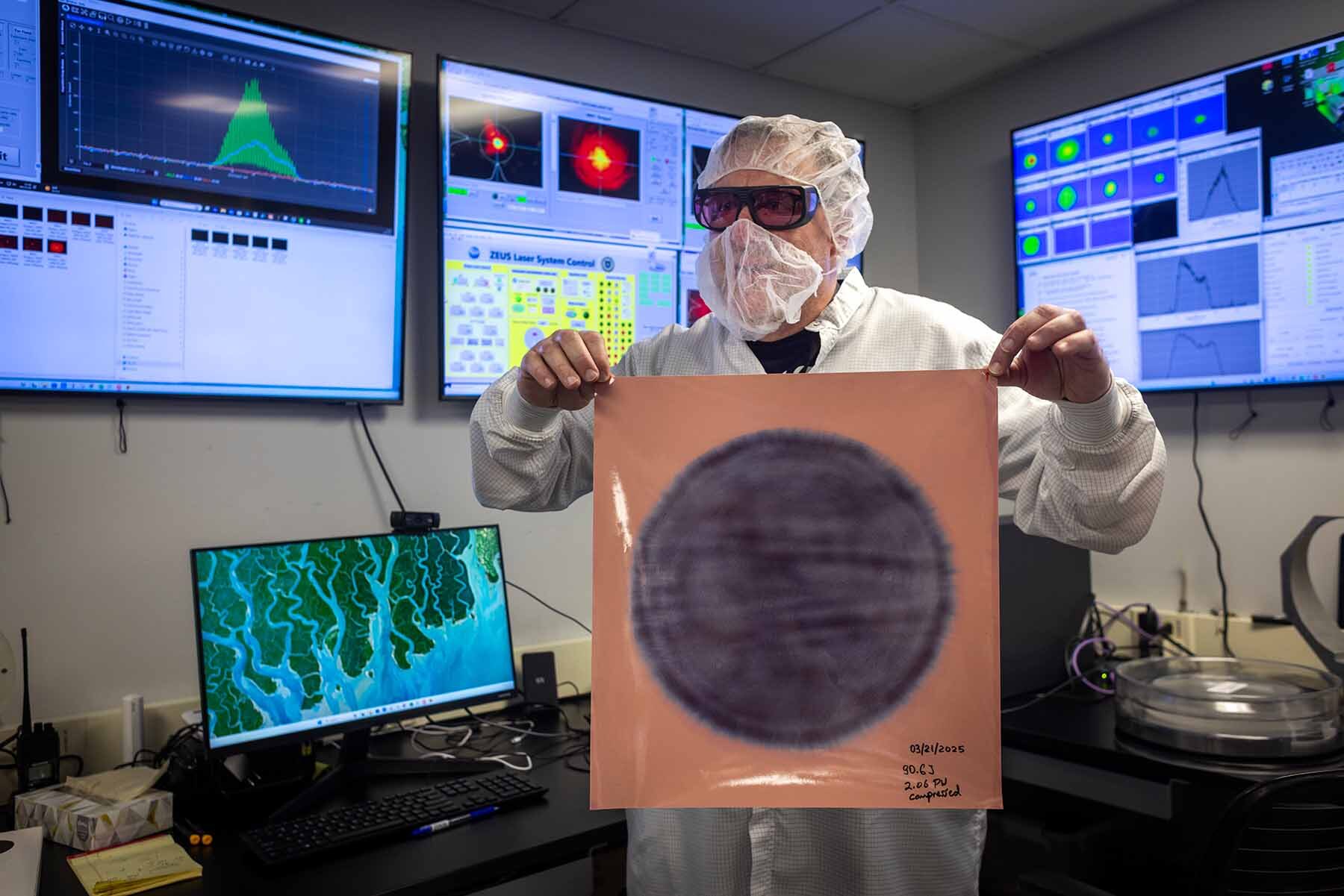 Gregg Sucha, laser engineer, holds up a laser burn mark on photographic paper in a control room of the ZEUS lab.