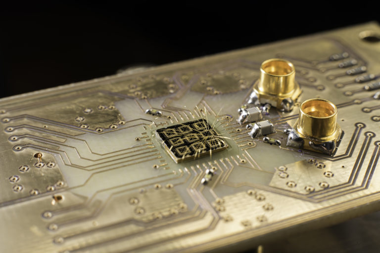 Thin aluminum wires connect the surface of a quantum processor semiconductor chip to pads on a circuit board.