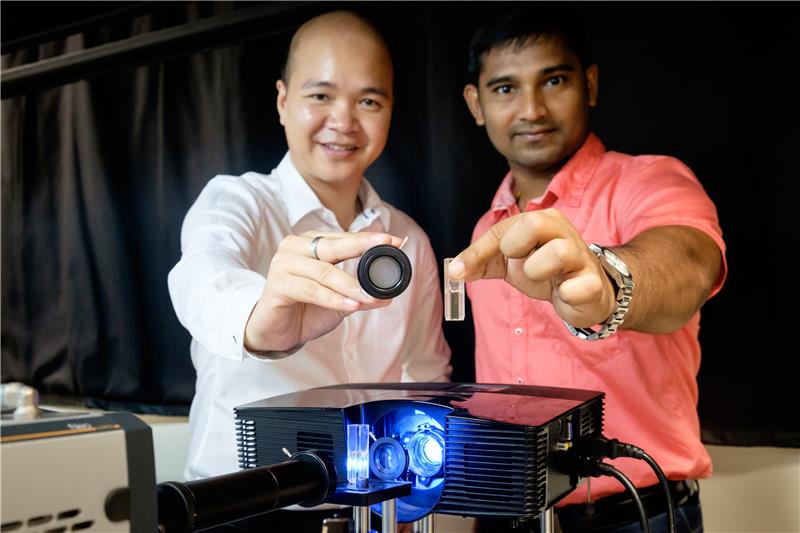 Asst Prof Steve Cuong Dang holding a tube with ground glass that can detect the difference in objects and Dr Sujit Kumar Sahoo holding a vial of apple juice