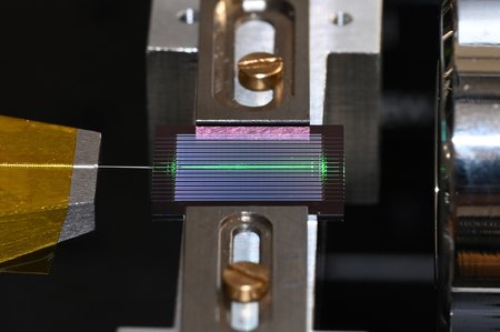 In this image, the chip includes ~20 OPOs, and one of them is being tested. An optical fiber is shown to the left of the chip and a free-space objective to the right.
